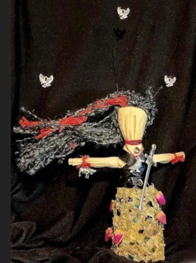 Doll of the M&oacute;rr&iacute;gan: black and grey yarn hair streaming back, with a small sword