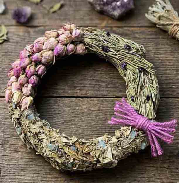Ostara wreath of silvery-green dried herbs and grasses with a cluster of pink rosebuds and a magenta twine bow